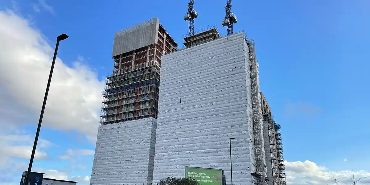 High-rise building under construction at The Perfume Factory site, covered in scaffolding and white protective wrap under blue sky