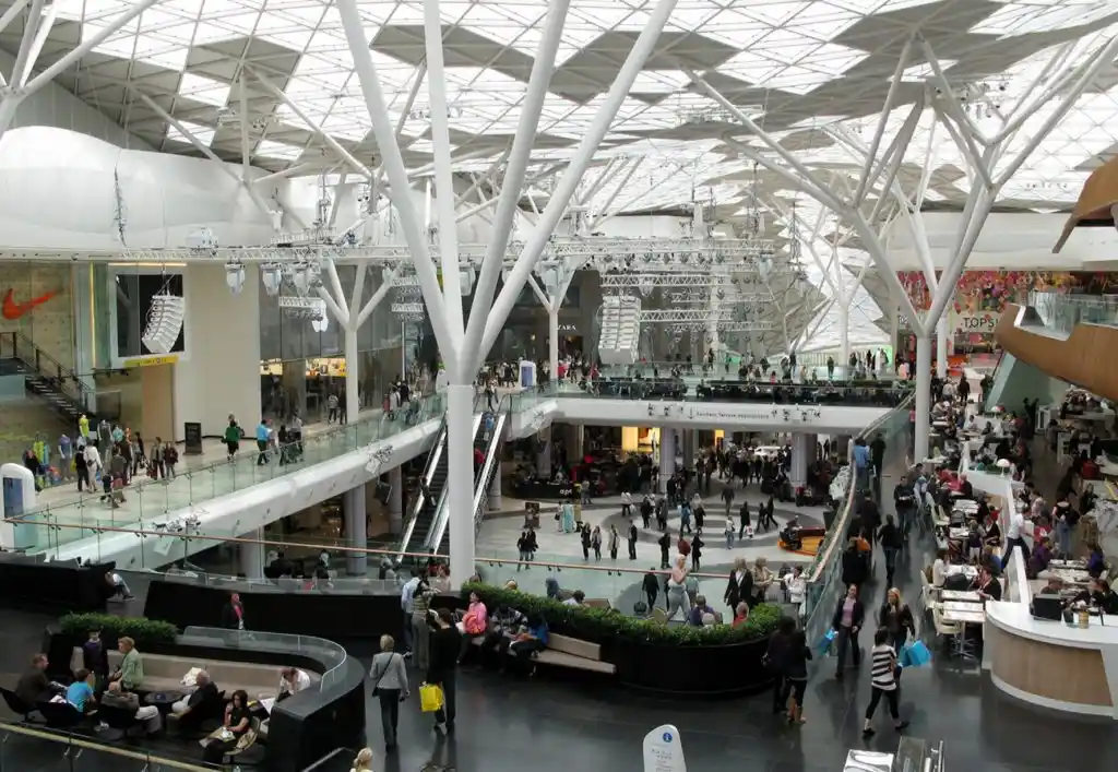Spacious multi-level shopping centre interior with large skylights and crowds of shoppers