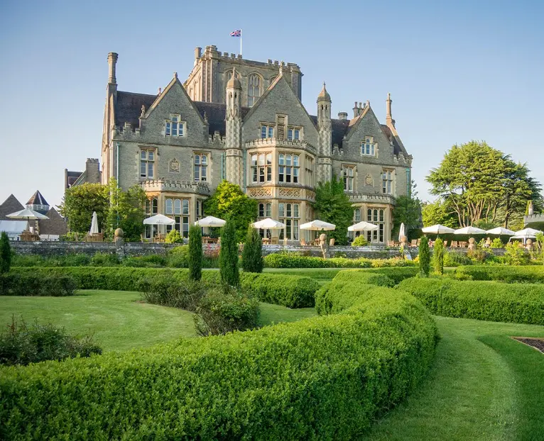 Historic British manor house with manicured garden and neatly trimmed hedges in the foreground, showcasing Cudd Bentley Consulting's commitment to integrating architectural heritage and landscape in sustainable building practices.