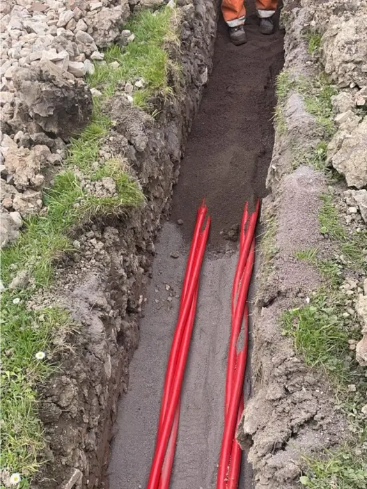 Close-up of utility service installation showing red conduit pipes laid in a prepared trench
